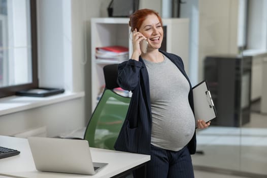 Pregnant woman using mobile phone and holding paper tablet in office