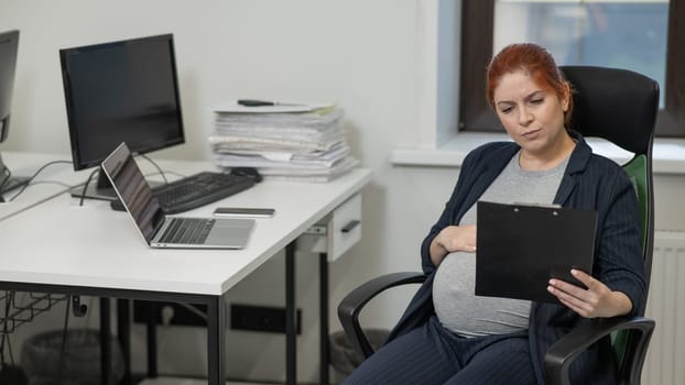 Pregnant woman reading documents on a paper tablet in the office