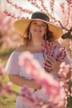 Woman blooming peach orchard. Against the backdrop of a picturesque peach orchard, a woman in a long white dress and hat enjoys a peaceful walk in the park, surrounded by the beauty of nature