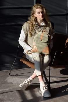 A woman holds leather backpack. Model wearing stylish knitted vest, white shirt and classic trousers.