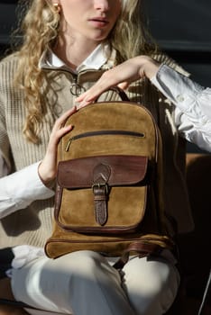 A woman holds leather backpack. Model wearing stylish knitted vest, white shirt and classic trousers.