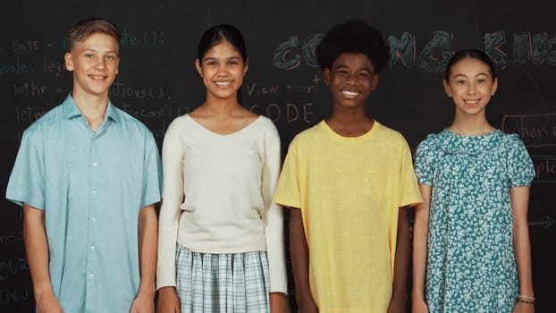 Group of smart multicultural teenager looking at camera at blackboard. Happy diverse children standing in STEM technology class with engineering code, prompt or planning program idea. Edification.