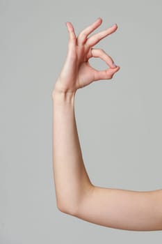 Female hand showing OK sign on gray background close up