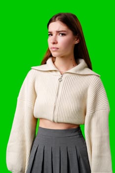 A young woman stands confidently against a vivid green background, dressed in a casual yet fashionable white cropped hoodie and a gray pleated skirt. Her expression is serene with a hint of contemplation, and her body language exudes a relaxed poise.