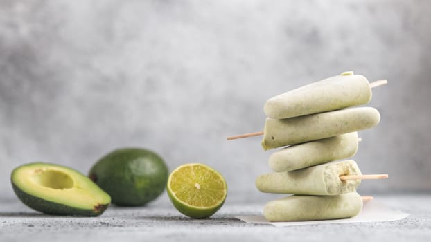 Homemade raw vegan avocado lime popsicle. Sugar-free, non-dairy green ice cream on gray cement textured background. Copy space. Ideas and recipes for healthy snack, dessert or smoothie. Banner