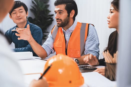 Diverse group of civil engineer and client working together on architectural project, reviewing construction plan and building blueprint at meeting table. Prudent