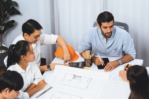 Diverse group of civil engineer and client working together on architectural project, reviewing construction plan and building blueprint at meeting table. Prudent