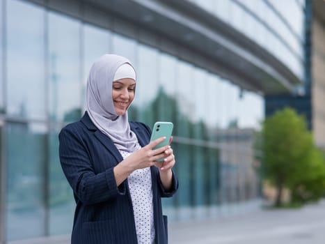 Business woman in hijab and suit using smartphone outdoors