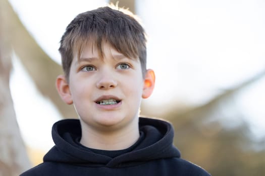 A boy with braces is smiling at the camera. The boy is wearing a black hoodie and has a greenish tint to his eyes