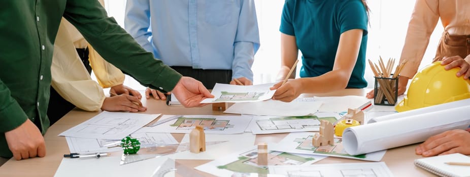 Professional architect engineer team discussion about architectural project on meeting table with wooden block and blueprint scatter around. Design and cooperate concept. Closeup. Delineation.