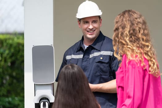 Technician install home EV charging station, providing service support for EV app on customer smartphone for monitoring charging status and set charging schedules at home. Synchronos