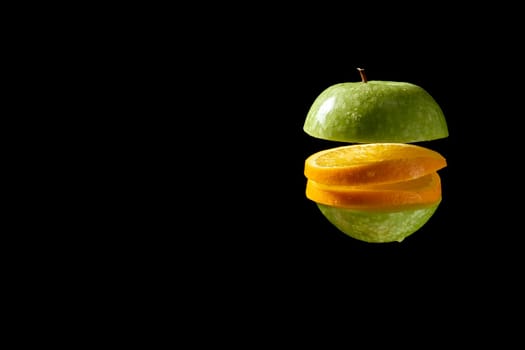 Close up of sliced green organic fresh apple and orange with water droplets on black background