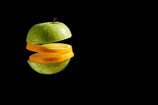 Close up of sliced green organic fresh apple and orange with water droplets on black background