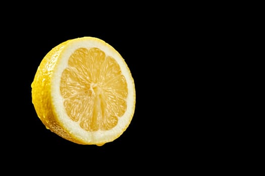 Closeup of fresh yellow organic half lemon with water droplets on black background