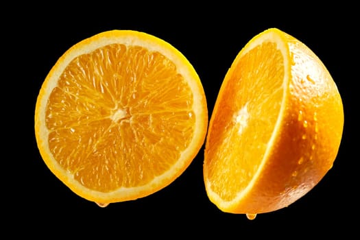 Two fresh halves of orange with water droplets on black background