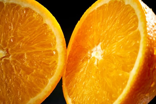 Two fresh halves of orange with water droplets on black background