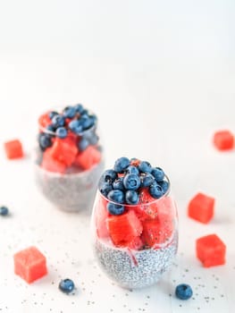 Healthy breakfast concept and idea - chia pudding with watermelon and blueberries. Two glass with chia pudding dressed watermelon and blueberry on white wooden tabletop. Copy space for text. Vertical.