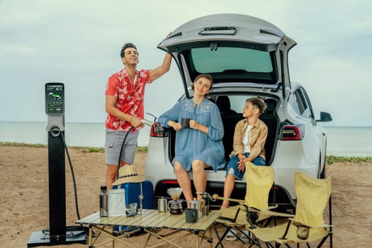 Family vacation trip traveling by the beach with electric car, happy family recharge EV car, enjoying outdoor camping coffee. Seascape travel and eco-friendly car for clean environment. Perpetual