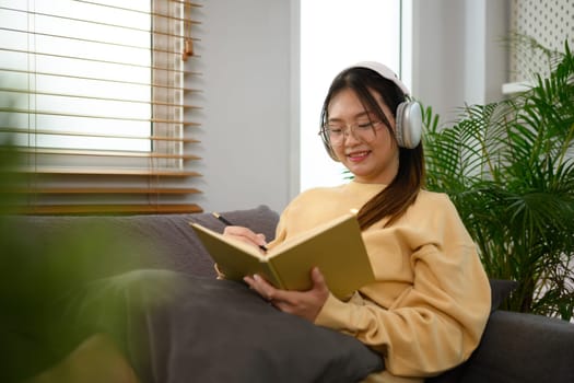 Pretty young woman listening to music with headphone and reading book at home.