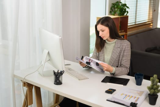 Young businesswoman looking at computer screen, working distantly at modern home office.