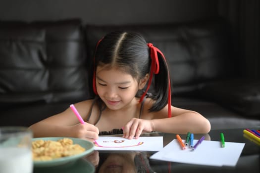 Cute young Asian girl drawing with colored pencil in living room.