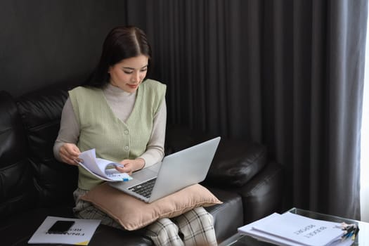 Young businesswoman sitting in modern living room and working with laptop. Remote work concept.