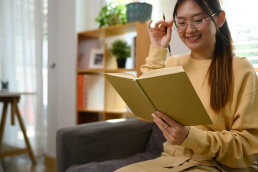 Pretty young woman listening to music with headphone and reading book at home.