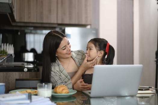 Beautiful working mom using a laptop and spending time with her little daughter at home.