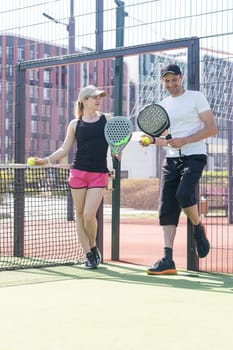 Cheerful athletic couple laughing during padel tennis match on outdoor court. High quality photo