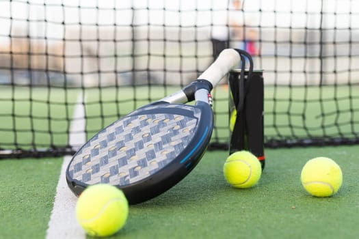 Blue padel racket and yellow balls placed on court near net on sunny day. High quality photo