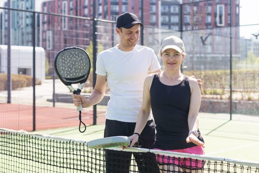 Sports couple with padel rackets posing on tennis court. High quality photo