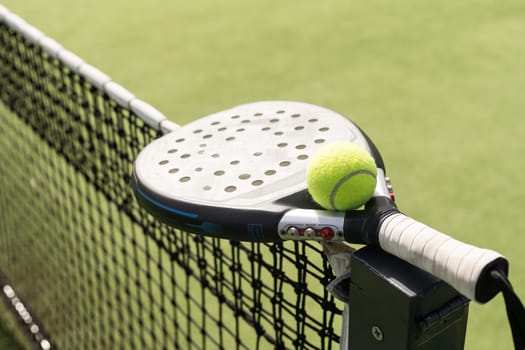 Padel racket and padel ball on a green court in the sunset. High quality photo