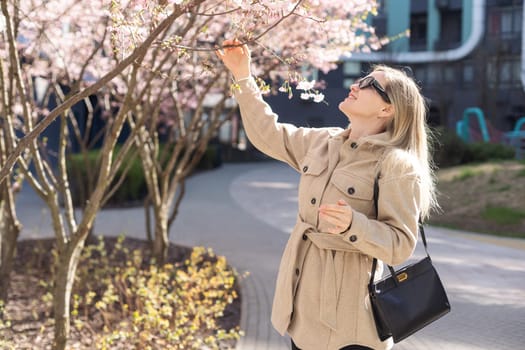 Sakura branches with flowers on a tree on the city streets. Happy woman girl in a gray palette walks along an alley with blooming sakura. Gorgeous fancy girl outdoors. Sakura tree blooming. High quality photo