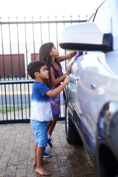 Children, car wash and helping siblings or outdoor together for to do list, discipline or teamwork. Boy, girl and cloth at transport in home driveway for cleaning responsibility, learning or task.