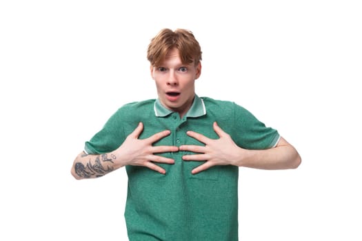 portrait of a surprised red-haired man in a green t-shirt with a tattoo on his arm on a white background with copy space.