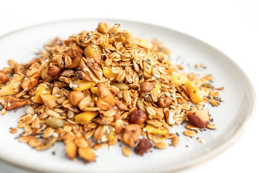 A bowl of granola with nuts and seeds on a white plate. The granola is a mix of different types of grains and nuts, and it looks like a healthy snack