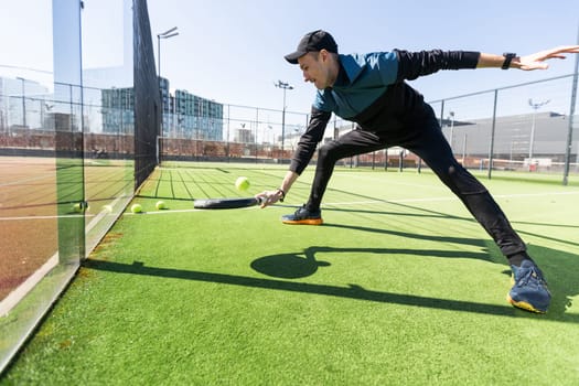 A padel player jump to the ball, good looking for posts and poster. Man with black racket playing a match in the open behind the net court outdoors. Professional sport concept with space for text. High quality photo