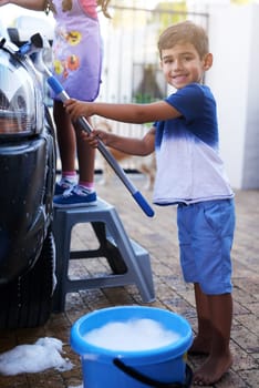 Child, portrait and washing car in home or cleaning responsibility for chore, task or helping. Boy, smile and bubble soap on vehicle for dirty transport or independence teamwork, learning or youth.