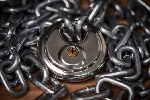 Security, steel and chain with lock for safety on wooden surface for privacy or protection. Metal, equipment and iron padlock and link shackles on table for password or guard with key for secret