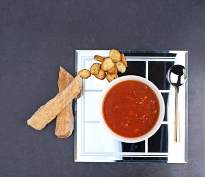 Tomato, soup and bread on menu in restaurant with bowl of healthy food for diet and nutrition benefits. Dinner, dish and luxury appetizer course in fine dining kitchen with breadsticks on plate.