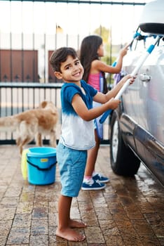 Children, portrait and home and washing car, kids and cleaning motor vehicle with equipment for fun. Siblings, driveway and helping with responsibility together on weekend, happy in outdoor for chore.