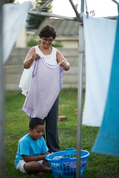 Outdoor, grandmother and grandchild with laundry, help and chore with summer and bonding together. Family, senior woman and boy with clean clothes and activity in backyard with washing and home.