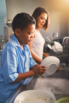Mother, son and dishes in kitchen with help or teamwork, tasks with collaboration in home. Woman, boy and cleaning plate in house with water and soap, working together or cooperation with happiness.
