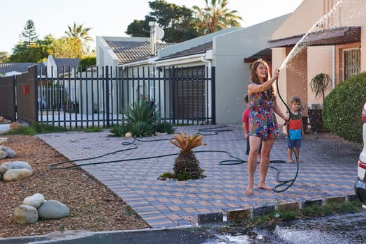 Children, mother and hose for car washing, cleaning and learning responsibility and development outdoor. Child or kid and mom for sibling, childhood and cute for water or fun on holiday for weekend.