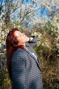 Beautiful red-haired woman enjoying smell in a flowering blooming spring garden. Spring blossom.