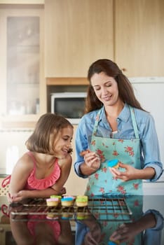 Mother, child and cupcakes baking in home or icing dessert as decorations, learning or bonding. Woman, daughter and teaching at kitchen counter for sweets snack or recipe support, helping or love.