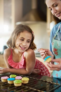 Mother, child and cupcakes baking in kitchen or icing dessert as decoration, learning or bonding. Woman, daughter and teaching in home for sweets snack or happiness kid for recipe, helping or candy.