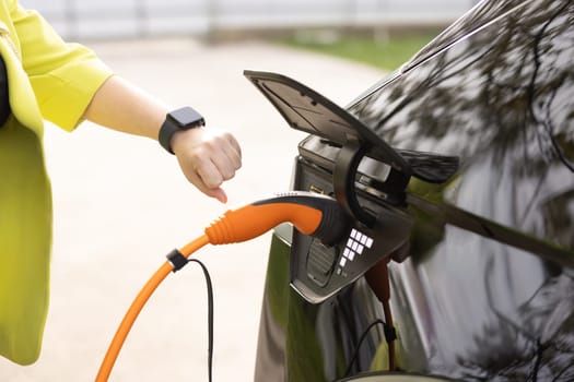 Female hands disconnects plug power cable. Unrecognizable woman unplugging electric car cable. Girl stopping charging using app on wearable smart watch. Eco friendly alternative energy transport.