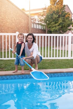 Mother, son and net for cleaning pool in backyard, chore and teaching kid responsibility in outdoors. Happy mommy, boy and help with housework or bonding in garden, toddler and support with learning.