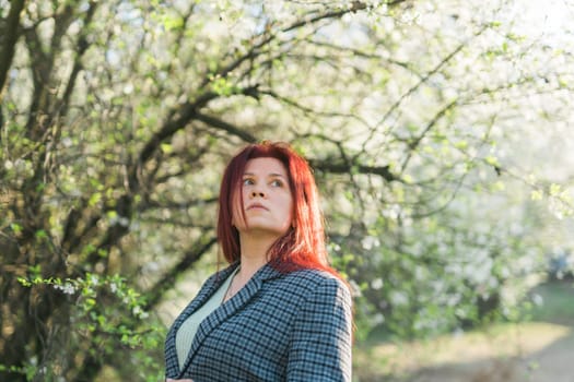 Beautiful red-haired woman enjoying smell in a flowering blooming spring garden. Spring blossom.